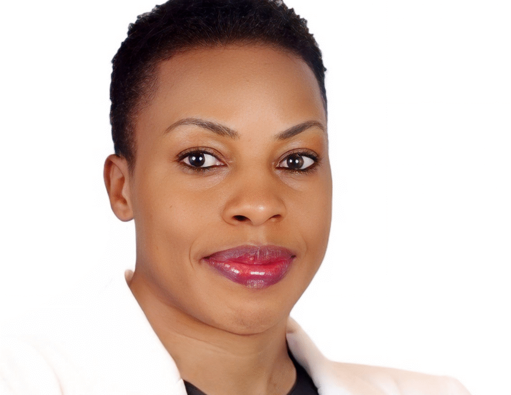 Portrait of Annet Birungi Petch wearing a white coat and black blouse, with short hair, smiling at the camera.