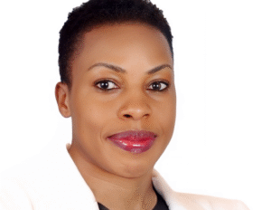 Annet Birungi Petch – Author Picture Portrait of Annet Birungi Petch wearing a white coat and black blouse, with short hair, smiling at the camera.